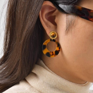 Close-up of tortoise shell resin hoop earrings with gold trim worn by a fashion model