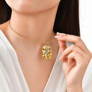Détail du pendentif carré doré avec rose argentée et texture plissée porté par le mannequin