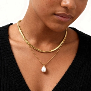 Close-up of a double-layered gold necklace with a water drop pearl pendant on a model