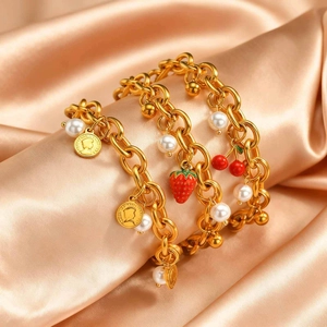 Dettaglio del bracciale dorato con perle finte, ciondoli a fragola e ciliegia e medaglia oro