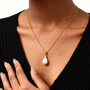 Macro shot of gold layered necklace with drop pearl pendant on a model wearing black V-neck