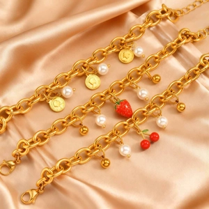 Vista macro di bracciali dorati con ciondoli a ciliegia, fragola e moneta della regina