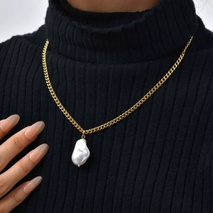 Close-up of golden flat cross chain with baroque pearl pendant on model's neck