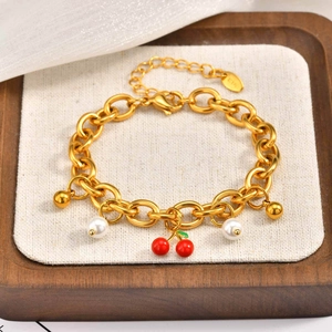 Dettaglio del bracciale a catena dorata con ciondoli a ciliegia, perle e sfere dorate su beige