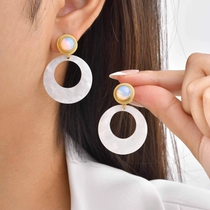 Detail view of gold drop earrings with white marble opal and acrylic ring on model