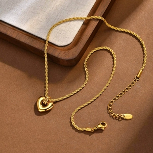 Détail de la chaîne torsadée dorée avec pendentif cœur et fermoir sur texture en bois