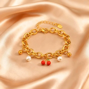Dettaglio del bracciale dorato con ciondoli a ciliegia e perle su seta champagne