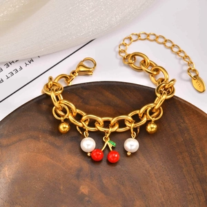 Dettaglio del bracciale dorato con ciondoli a ciliegia rossi, perle bianche e sfere d'oro