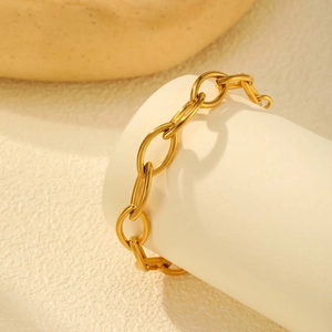 Bracciale a maglie ovali dorate geometriche su un piedistallo di pietra minimalista