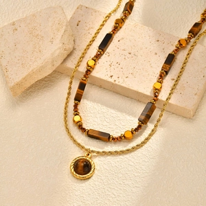 Détail de la chaîne dorée torsadée et pendentif oeil de tigre sur pierre de travertin