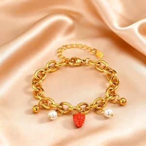 Dettaglio del bracciale a catena dorata con fragola e perle su fondo di raso