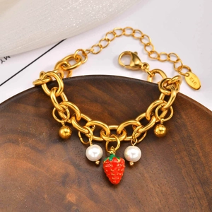 Dettaglio di bracciale dorato con fragola rossa, perle e punzonatura K18 su legno