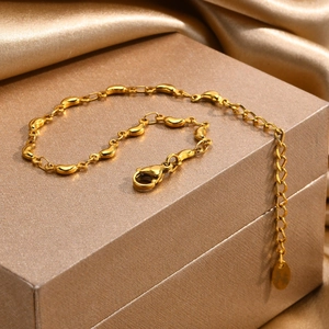 Detailed close-up of 18K gold bean charm bracelet with lobster clasp and extender