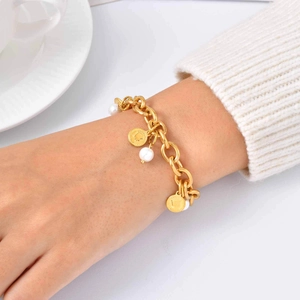 Dettaglio di un bracciale a catena dorata con perle bianche e ciondoli a moneta al polso