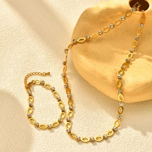 Detail van vergulde kettingset met ovale schakels en heldere strasstenen op luxe ondergrond
