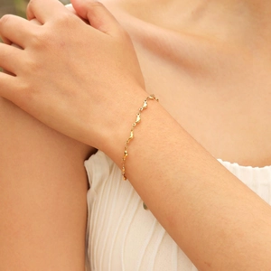Close-up of 18K gold dolphin pendant bracelet on wrist with tiny metal charms