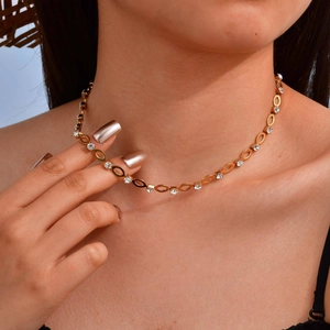 Detail van een goudkleurige ketting met ovale schakels en heldere strassteentjes op de nek