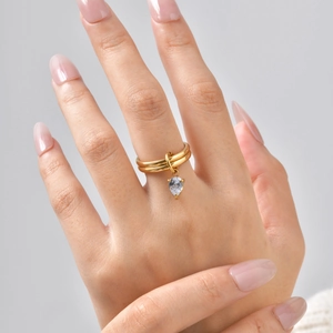 Détail d'une bague double dorée avec un pendentif en zircon blanc taillé en forme de poire