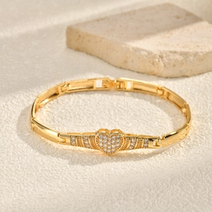 Detailed close-up of a gold heart bracelet with zircon stones on a sandy stone surface