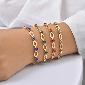 Detailopname van vier gouden armbanden met ovale schakels en gekleurde strasstenen