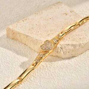 Detailed close-up of golden heart-shaped bracelet with cubic zirconia on stone background