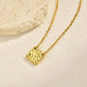 Détail d'un pendentif carré doré avec texture martelée sur fond de pierre beige
