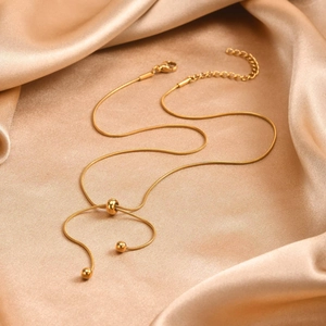 Golden stainless steel snake chain necklace with smooth metallic bead accents on silk