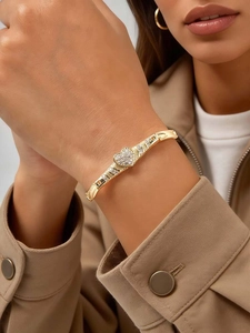 Detail of a gold-plated heart-shaped zircon bracelet on a woman wearing a trench coat