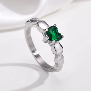 Gros plan d'une bague avec gemme verte en cœur et anneau argenté aux détails texturés