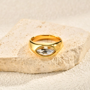 Golden wide band ring with a large marquise-cut white zircon on a stone background