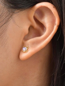 Détail d'une boucle d'oreille chat dorée avec opale sur le lobe d'une personne