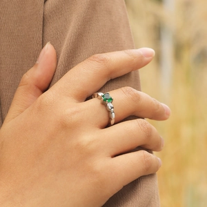 Gros plan sur bague cœur avec zircon vert et anneau argenté aux bords ondulés