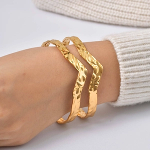 Vue détaillée de bracelets dorés en forme de V texturés sur le poignet d'un mannequin