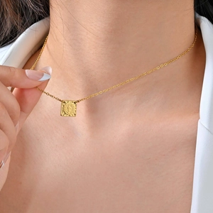 Gros plan du collier pendentif carré Saint-Benoît doré porté sur un blazer blanc