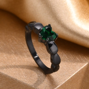 Détail macro d'une bague noire avec zircon vert en forme de cœur et anneau style chaîne