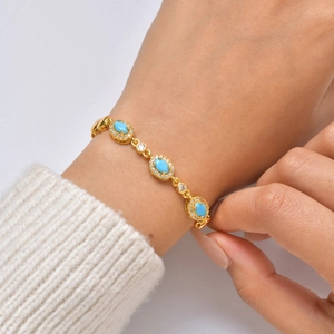 Dettaglio di bracciale placcato oro 24K con pietre turchesi su un maglione bianco