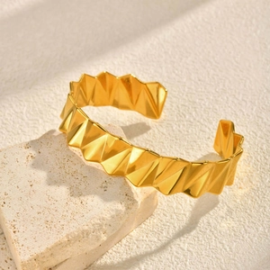 Détail d'un bracelet doré en V montrant une texture ondulée sur un support en pierre