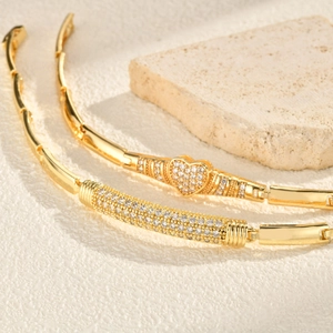 Gold heart and curved bar bracelets with pavé zircons on a textured stone surface