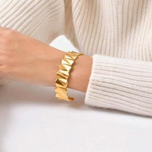 Détail d'un bracelet jonc doré en forme de V ondulé porté sur un pull blanc doux