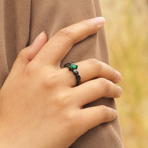 Détail d'une bague vintage noire avec pierre verte en forme de cœur sur la main d'un modèle
