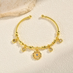 Detail of gold open bangle with woven texture featuring evil eye and zircon charms