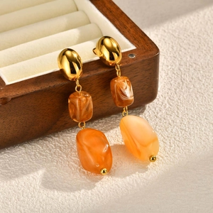 Detail of gold oval studs with marble brown and amber resin charms on wooden box