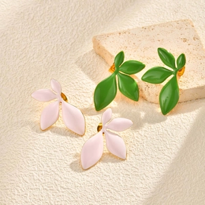 Close-up of leaf-shaped enamel earrings in pink and green on a textured stone