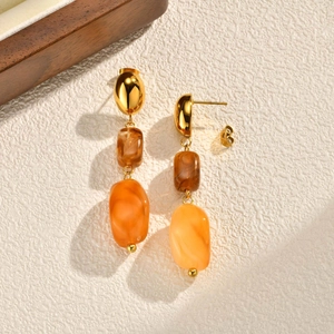 Detail view of gold metal earrings with amber resin beads on a textured surface