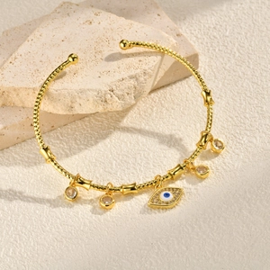 Detailed close-up of golden open bangle featuring evil eye and zircon charms on stone