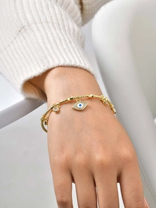 Macro detail of gold evil eye bracelet with blue zircon accents on a soft knit background