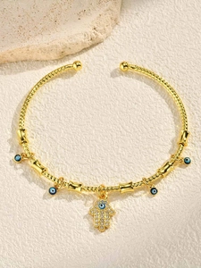 Detailed view of gold Hamsa hand and evil eye charms on a textured cuff bracelet