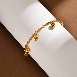 Golden stainless steel chain bracelet with polished heart and ball charms on display
