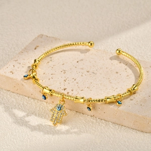 Detailed shot of gold Hamsa hand and blue Evil Eye charms on an open bangle bracelet