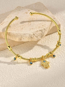 Detailed view of gold Hamsa Hand and Evil Eye charms on woven texture open bangle